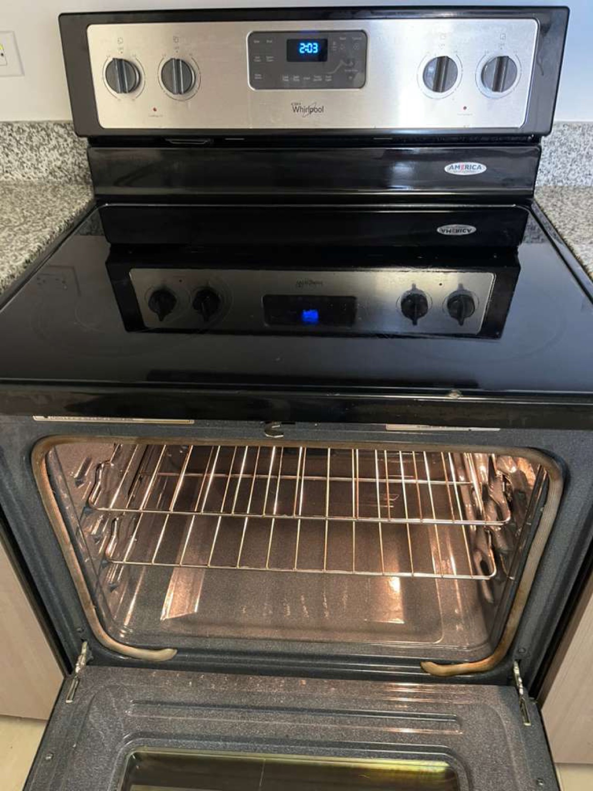The same Whirlpool electric range after cleaning, framed closer: cooktop glass clear, oven floor and walls clean, racks bright, inner door clean